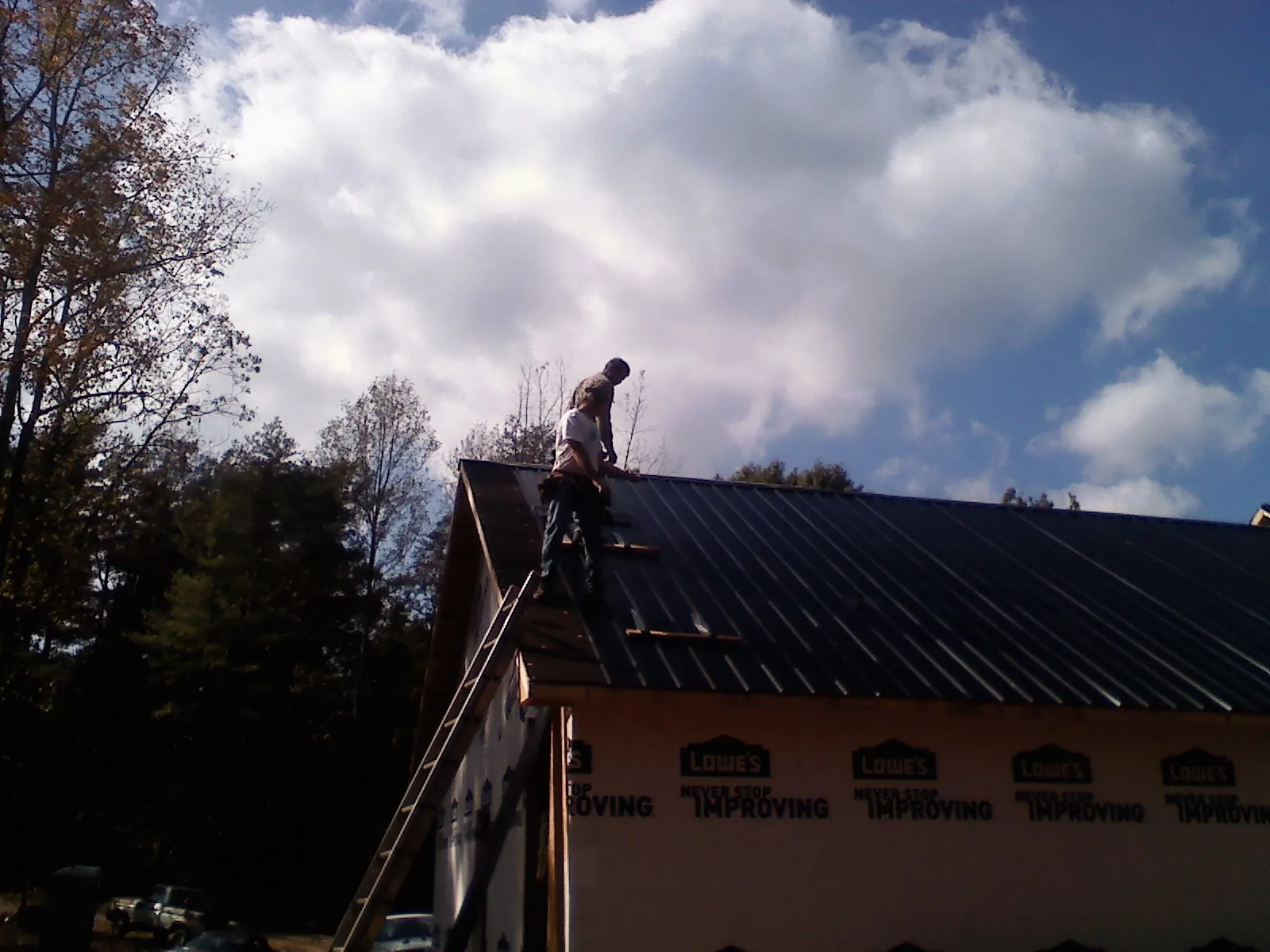 Roofer fastening dark metal panels high against a cloudy sky, from a Roof Inspection job in Blue Island