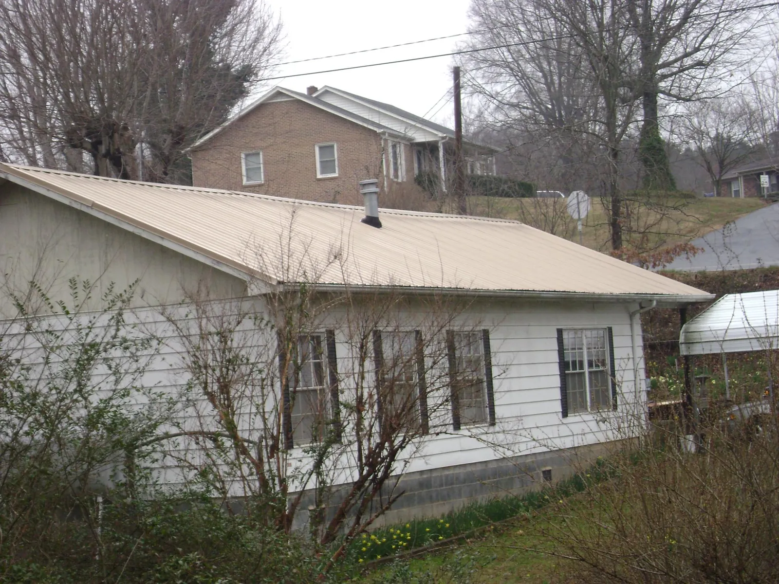 Tan metal roof on a white sided house set into a hillside — Commercial Roofing by Roofing Brothers in Blue Island